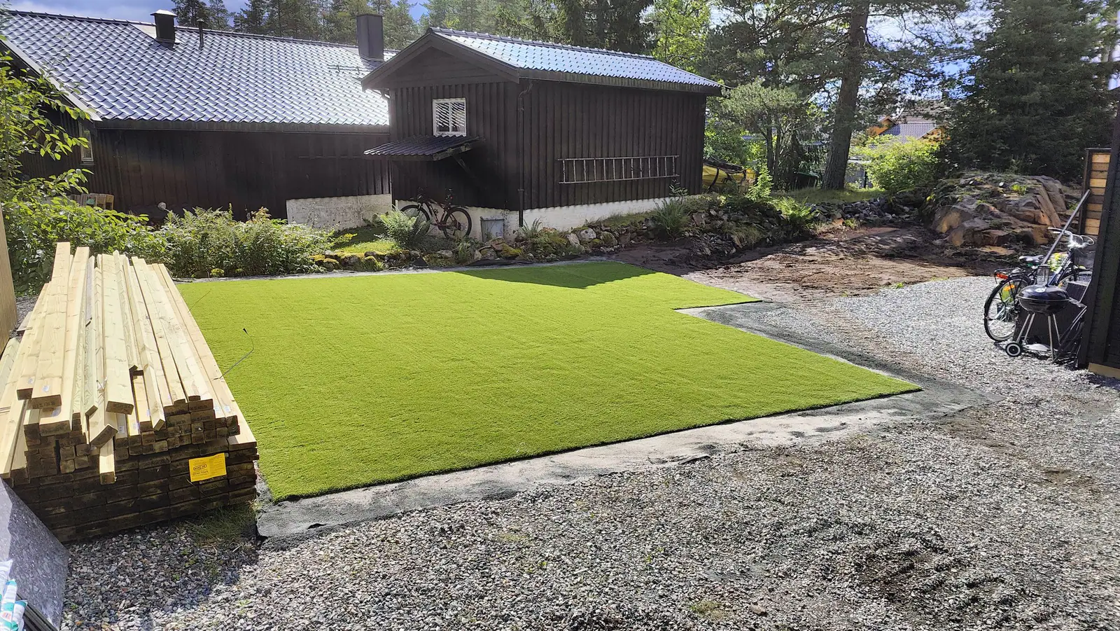 Nytt kunstgress lagt av Best Miljø i hage foran mørkt trehus, med grus rundt
